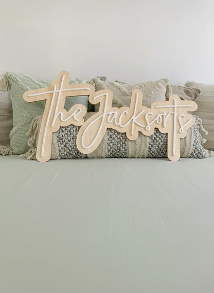 Wooden last name sign 'The Jacksorts' on a decorative pillow with a neutral background
