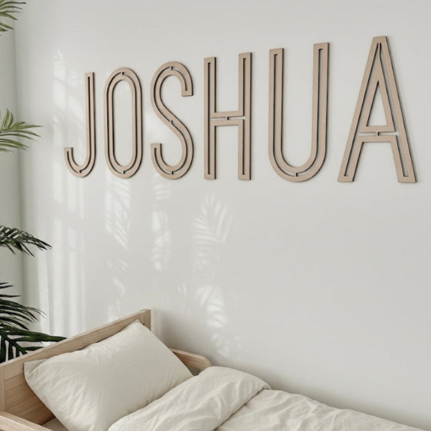 Wooden name 'JOSHUA' on a wall above a bed with white bedding.